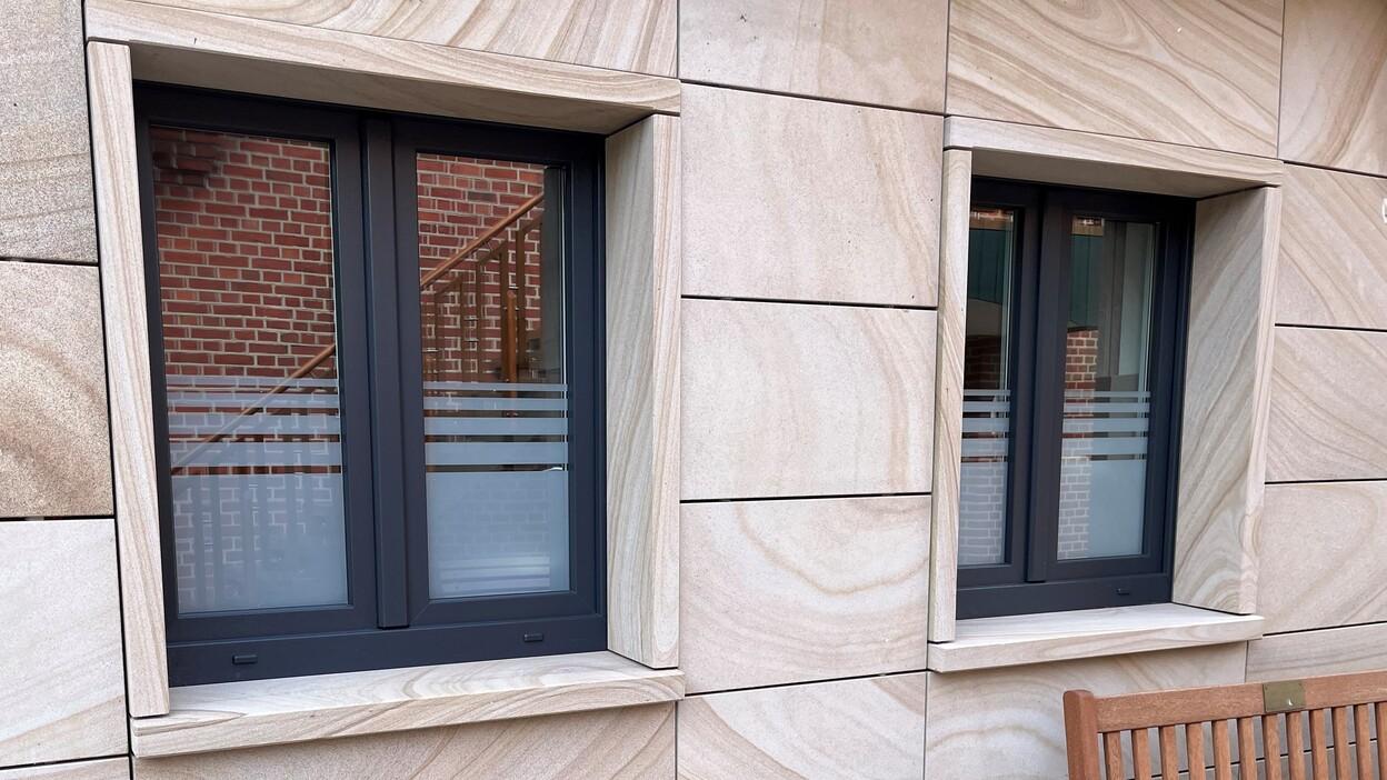 Fenster nach Maß Maßgefertigte moderne Fenster mit schwarzem Rahmen in Sandsteinfassade und Blumendekoration.