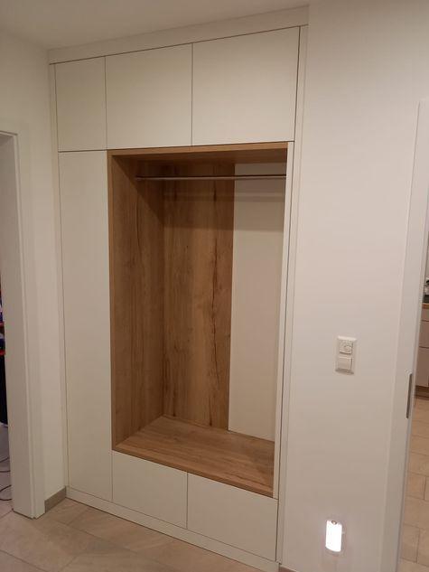 Individuelle Garderobe nach Maß mit Sitzbank, Holzrückwand und praktischen Stauraumfächern.