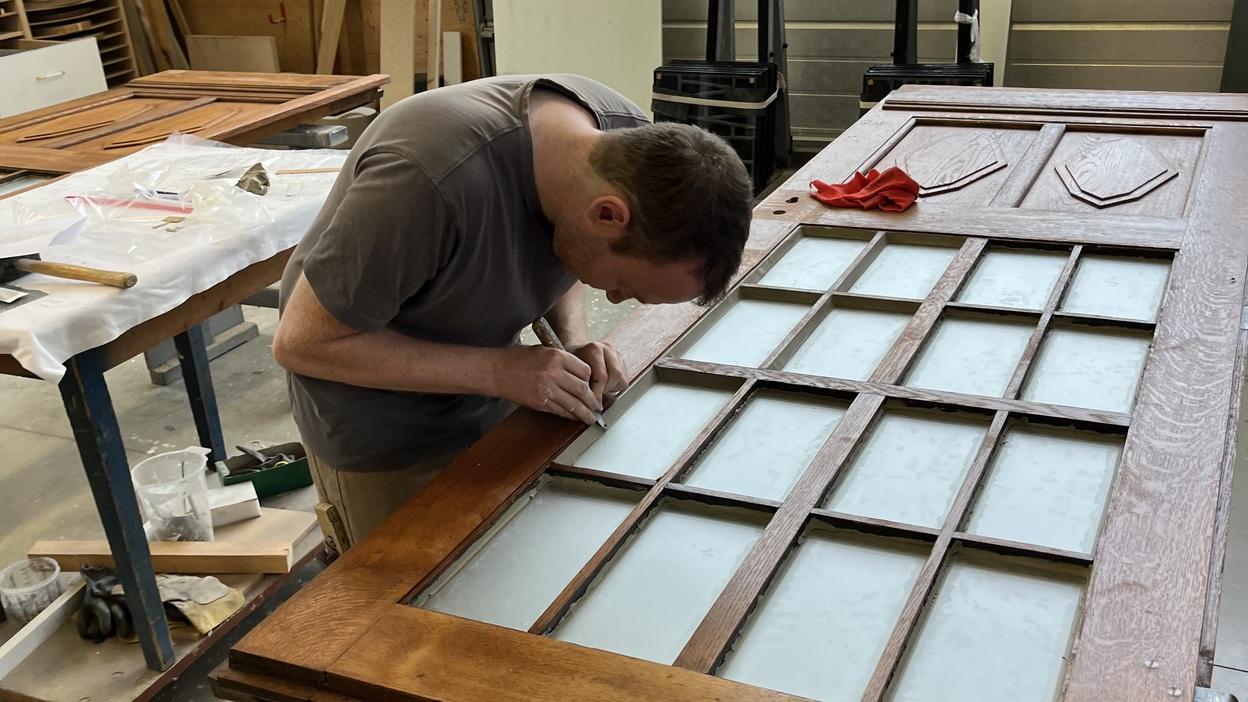 Holztür Restaurierung Werkstatt Handwerker restauriert alte Holztür mit Glaseinsätzen sorgfältig in traditioneller Werkstatt.