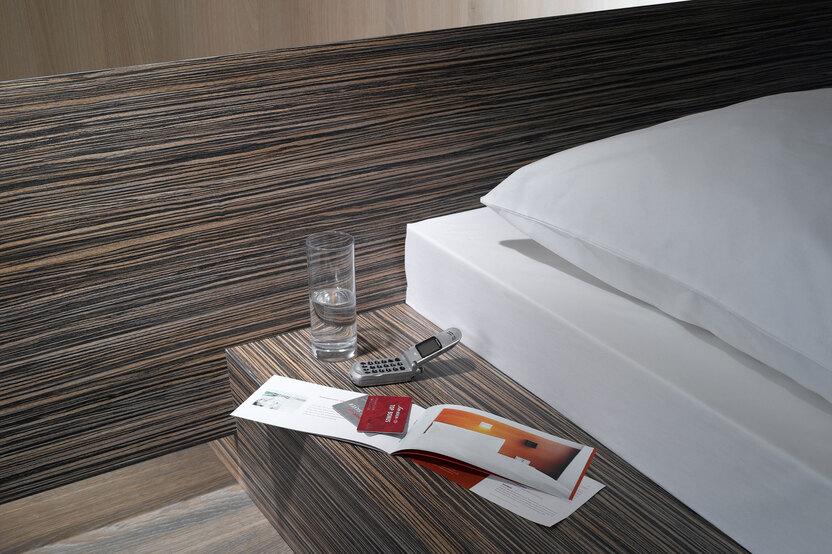 Detailaufnahme von Bettumrandung in dunklem Holz mit Ablagem&ouml;glichkeit